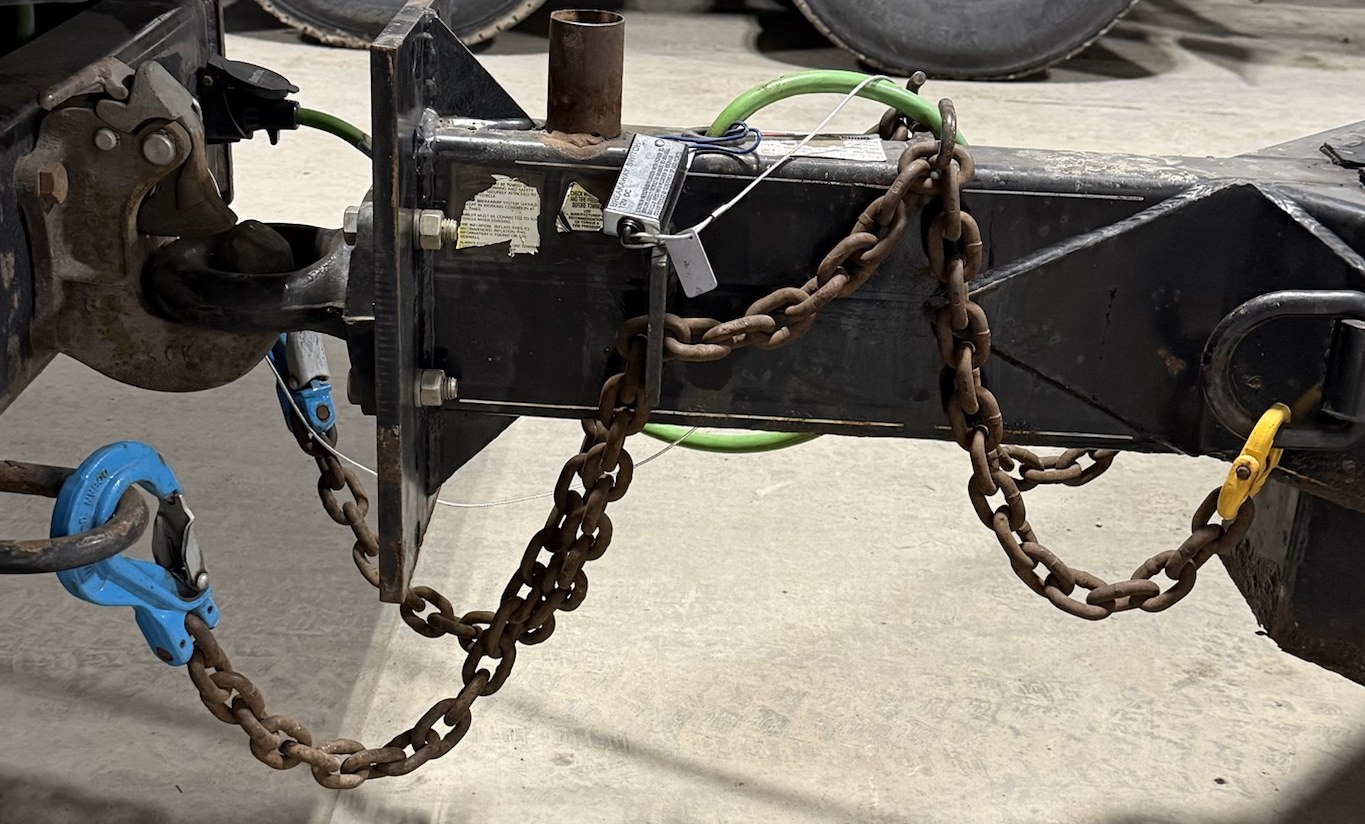 Pintle hook and lunette ring coupled on a heavy-duty equipment trailer, with safety chains, a breakaway switch and green wiring