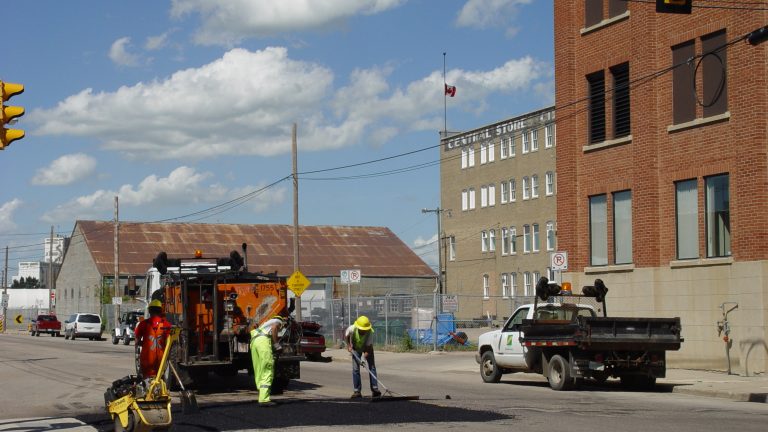 Road crew in high-visibility clothing repairing pavement beside a work truck on a city street