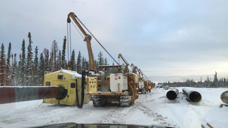 Pipeline crew in winter: side-boom tractors lined up beside lengths of pipe on a snowy right-of-way
