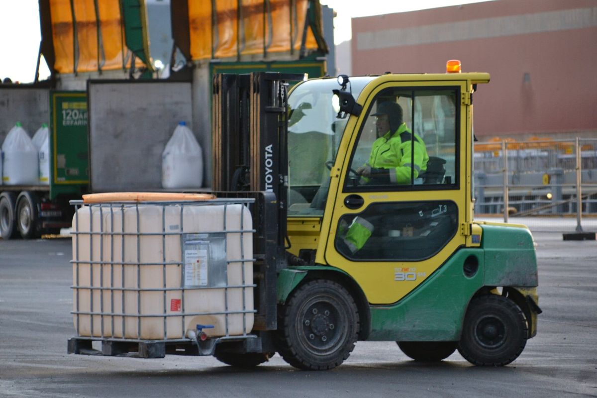 Forklift operator in a hi-vis vest moving a liquid tote