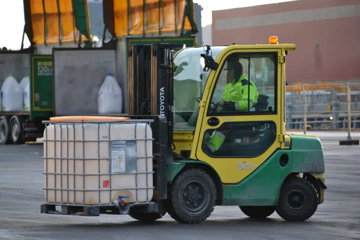 Forklift operator in a hi-vis vest moving a liquid tote