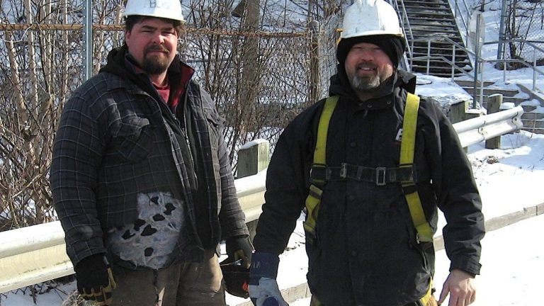 Two workers in hard hats and winter clothing on a snowy job site
