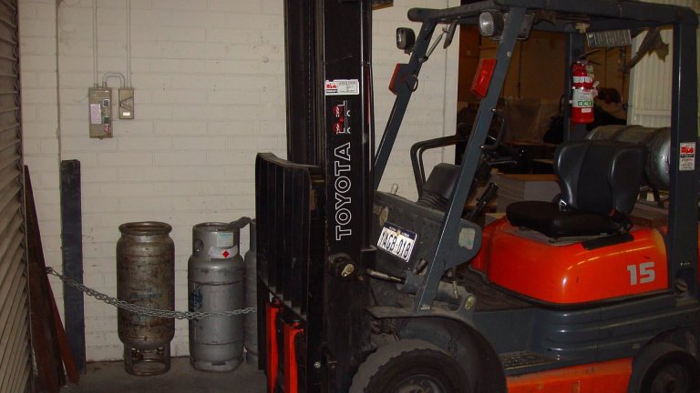 Forklift beside propane cylinders chained upright in a storage area