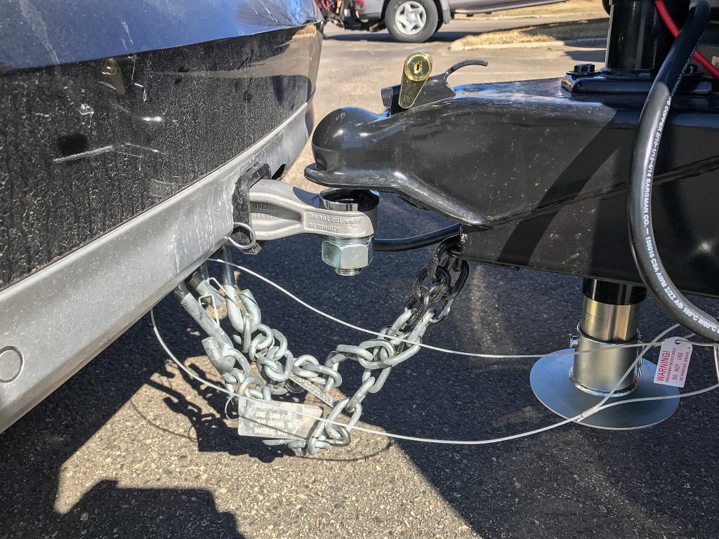 Close-up of a trailer coupler on a ball hitch with crossed safety chains, a tongue jack and wiring