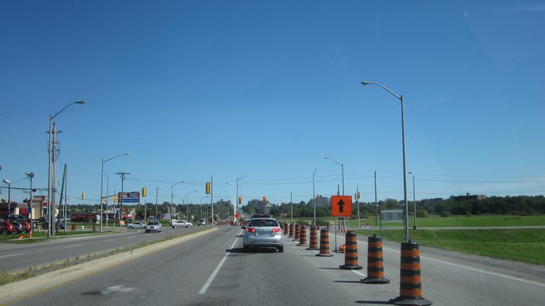 Orange and black construction barrels closing a lane on a four-lane highway