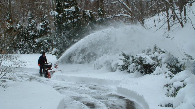 Operator clearing a long driveway with a walk-behind snow blower