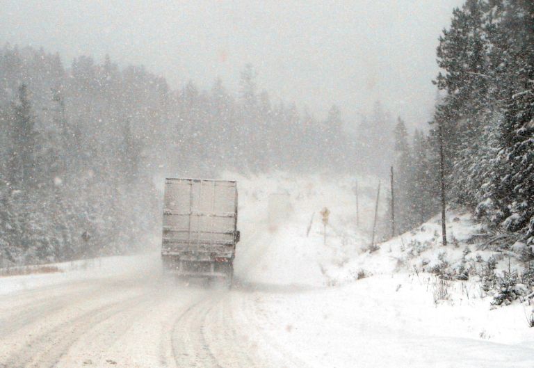 Transport truck driving through a snowstorm on a forested highway